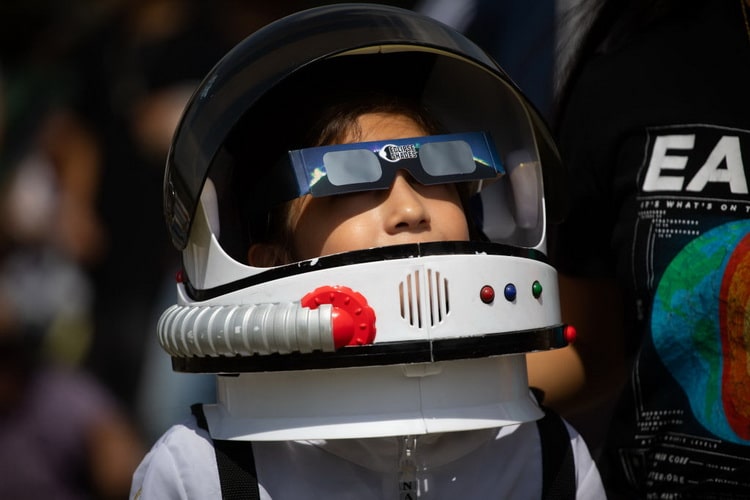 کودکی در حالی که لباس فضانوردی به تن دارد از خورشیدگرفتگی لذت می برد.
